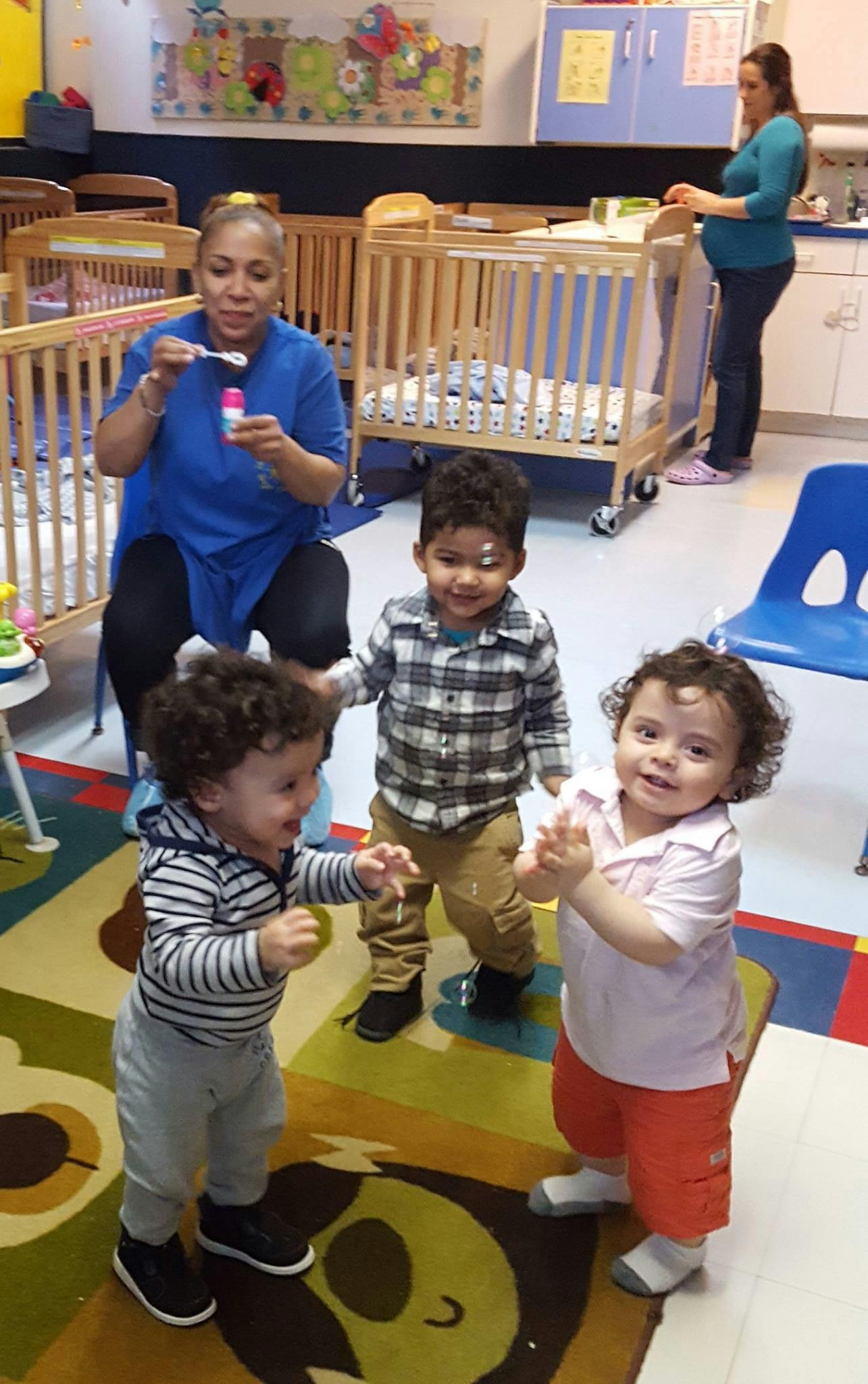 Person blowing bubbles for three children in a classroom