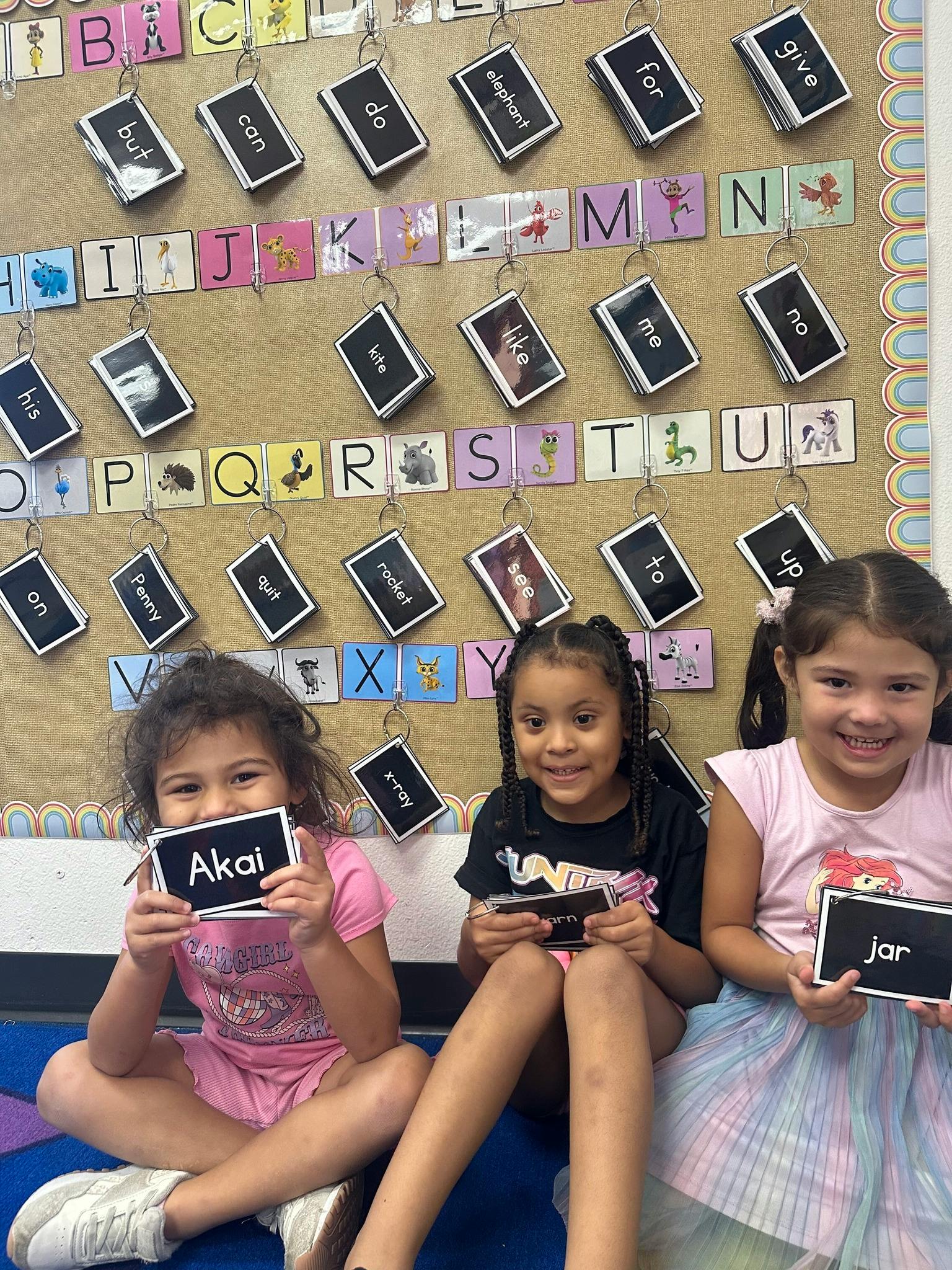 Three children sitting on the floor holding up flashcards