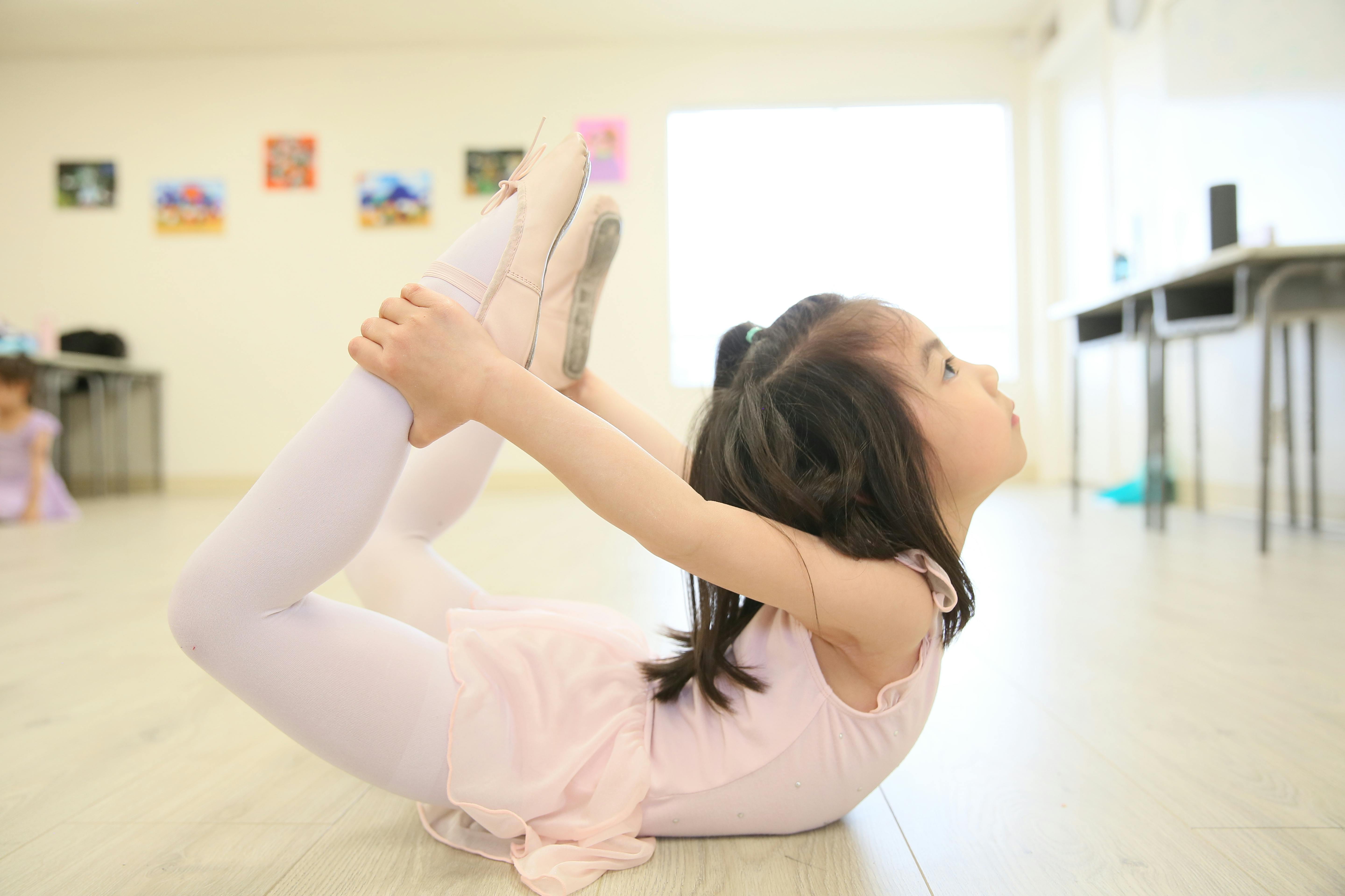 Child in ballet attire stretching on the floor