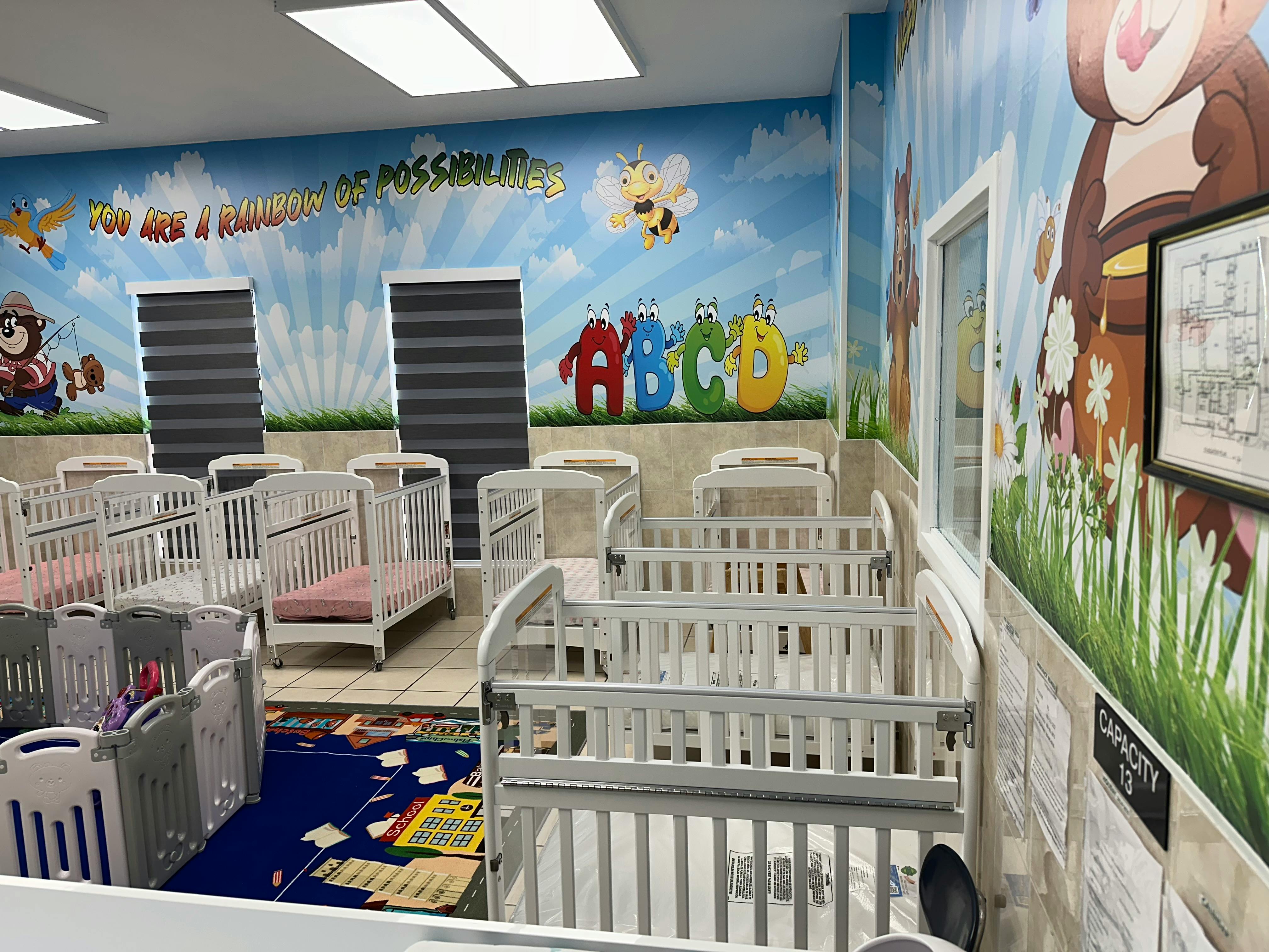 Room with multiple white cribs and colorful wall murals
