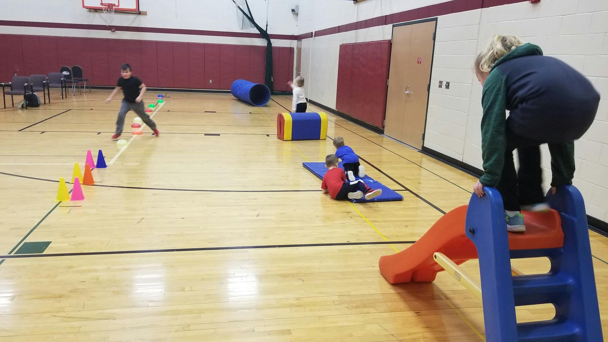 Children playing in a gym with a slide, cones, and tunnel
