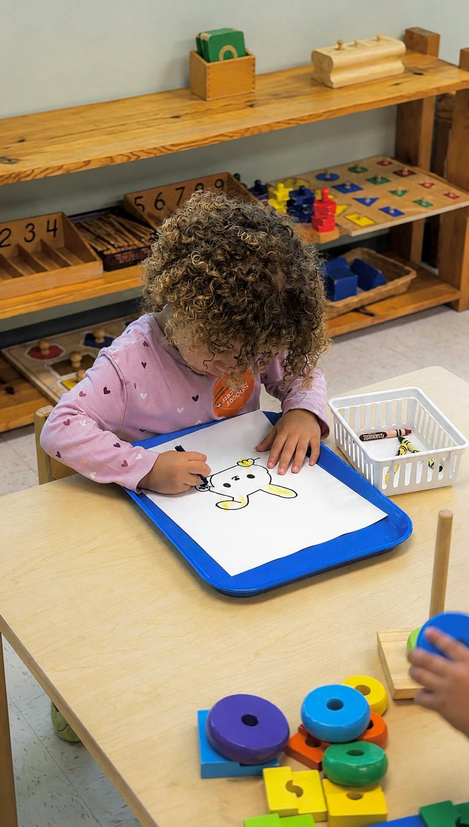 Child coloring a drawing of a rabbit on a tray at a table