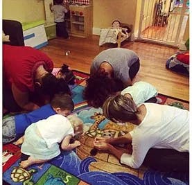 Adults and children kneeling on a rug, looking at a book