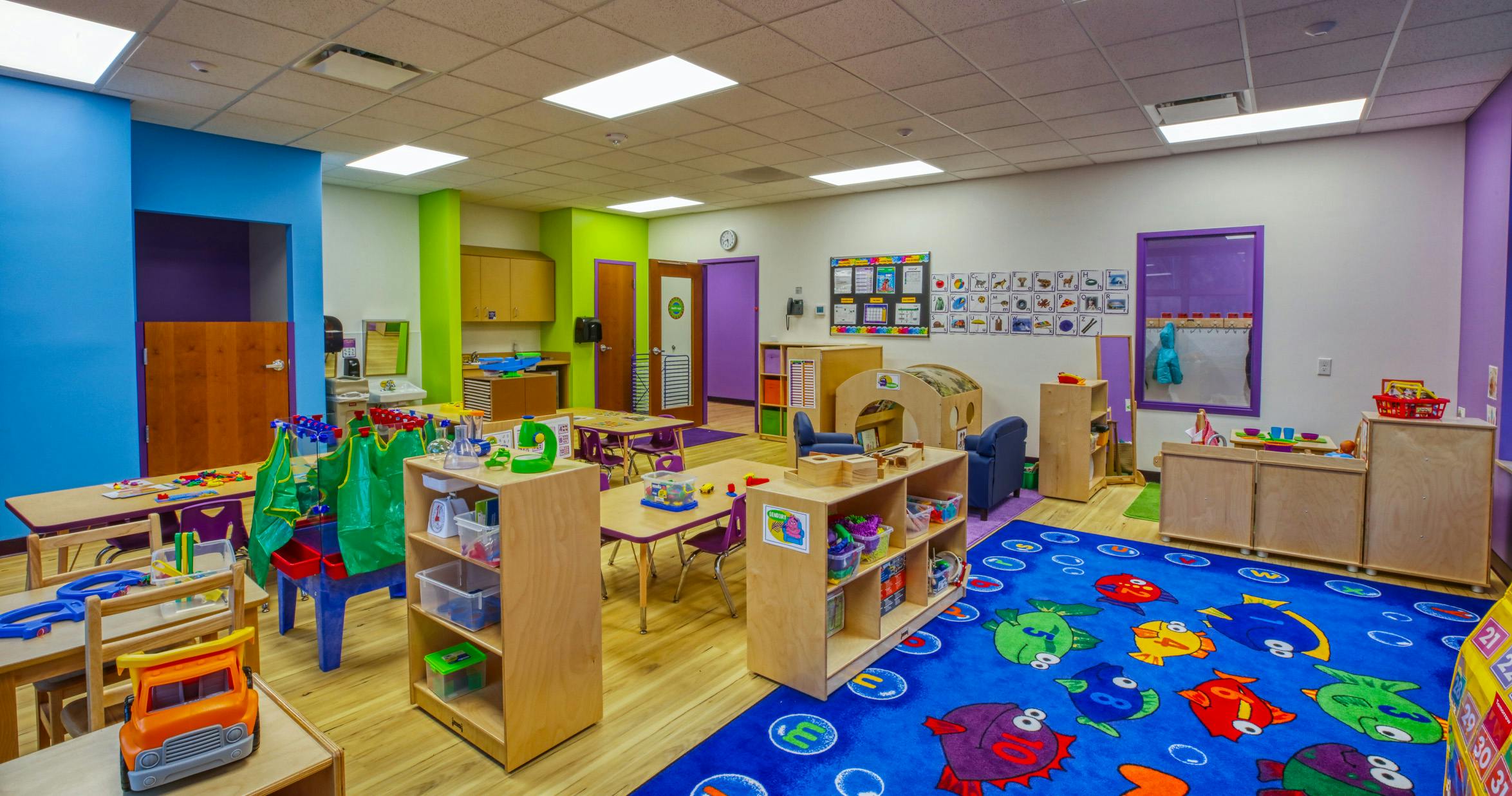 An empty early childhood classroom with colorful walls and a fish-themed rug