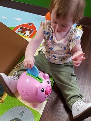 Child playing with a pink toy piggy bank