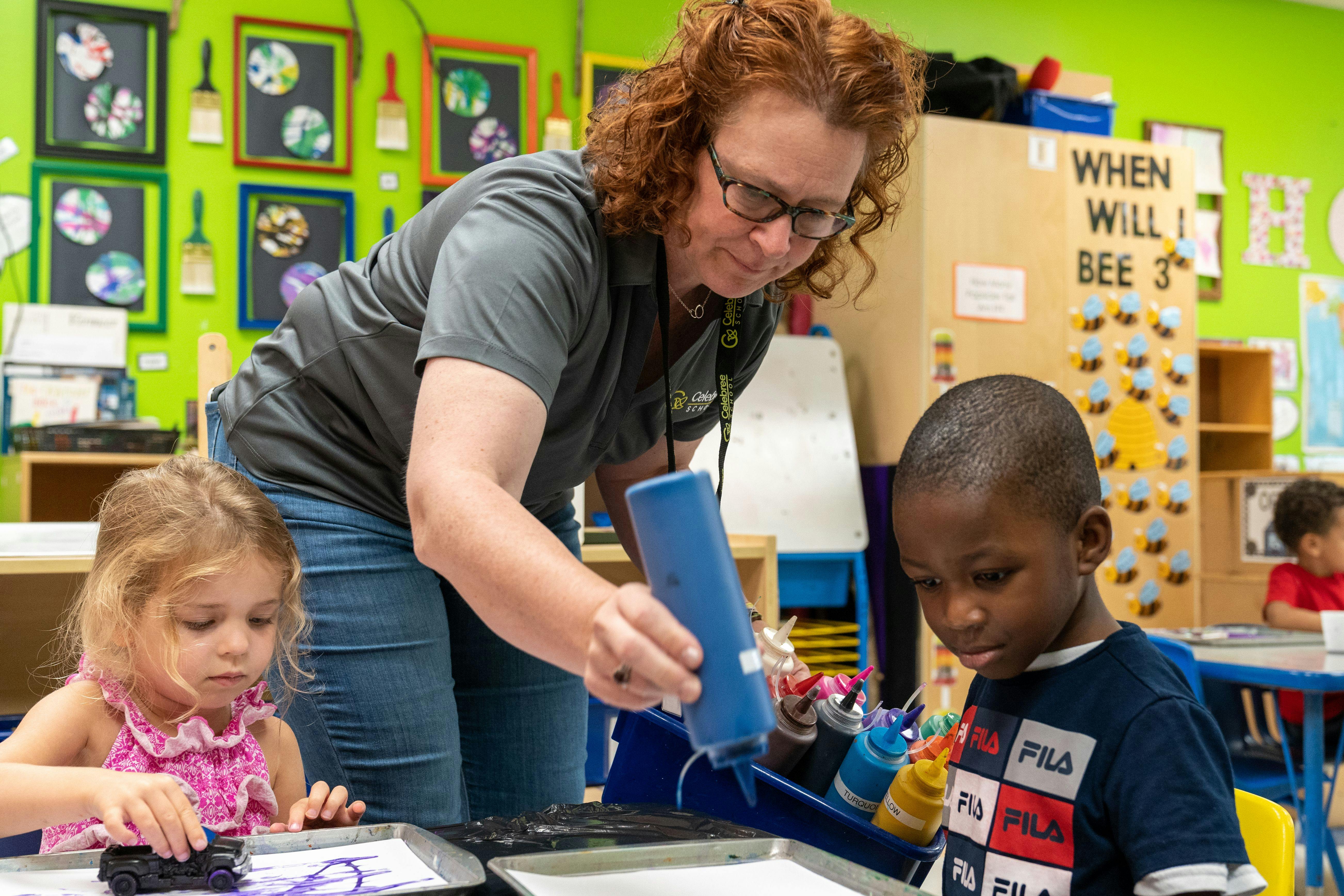 Adult helping two children with an art project in a classroom
