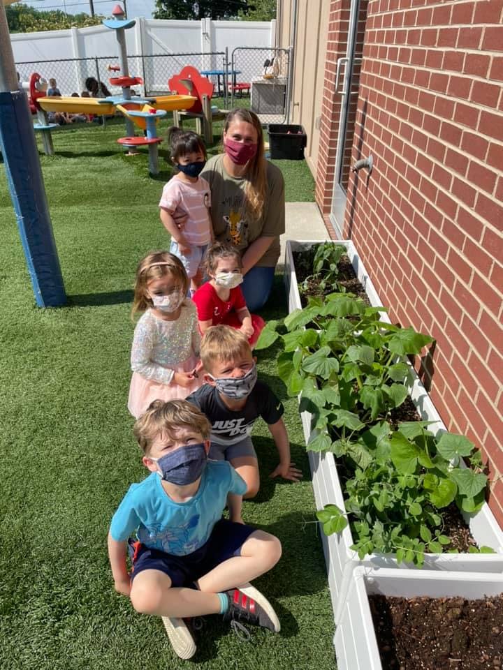 Adult and children in masks sitting by a planter box with plants