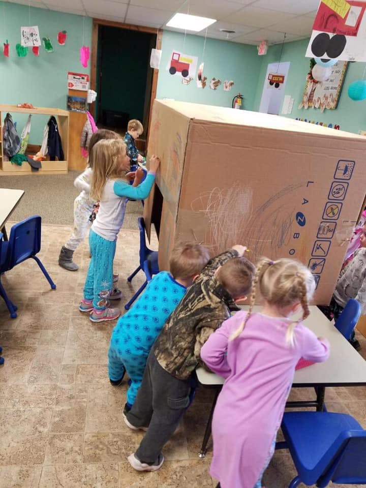 Children drawing on a large cardboard box in a classroom