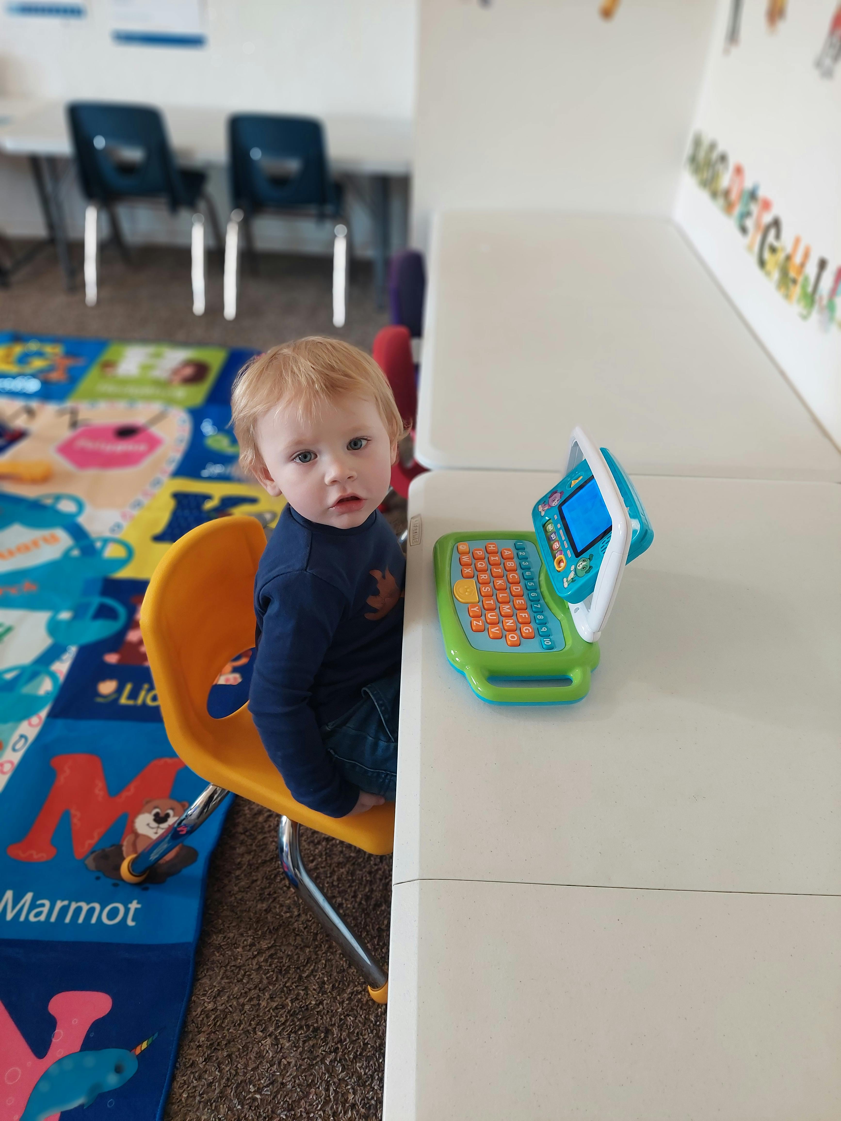 Child sitting at a table with a toy laptop