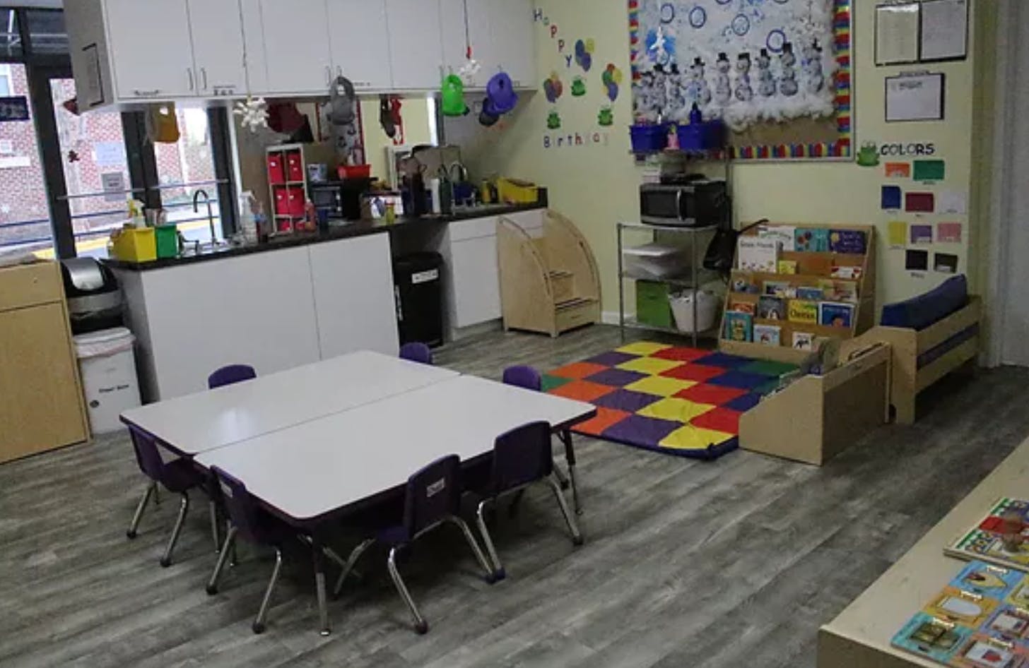 Classroom with small tables and chairs, colorful rug, and shelves