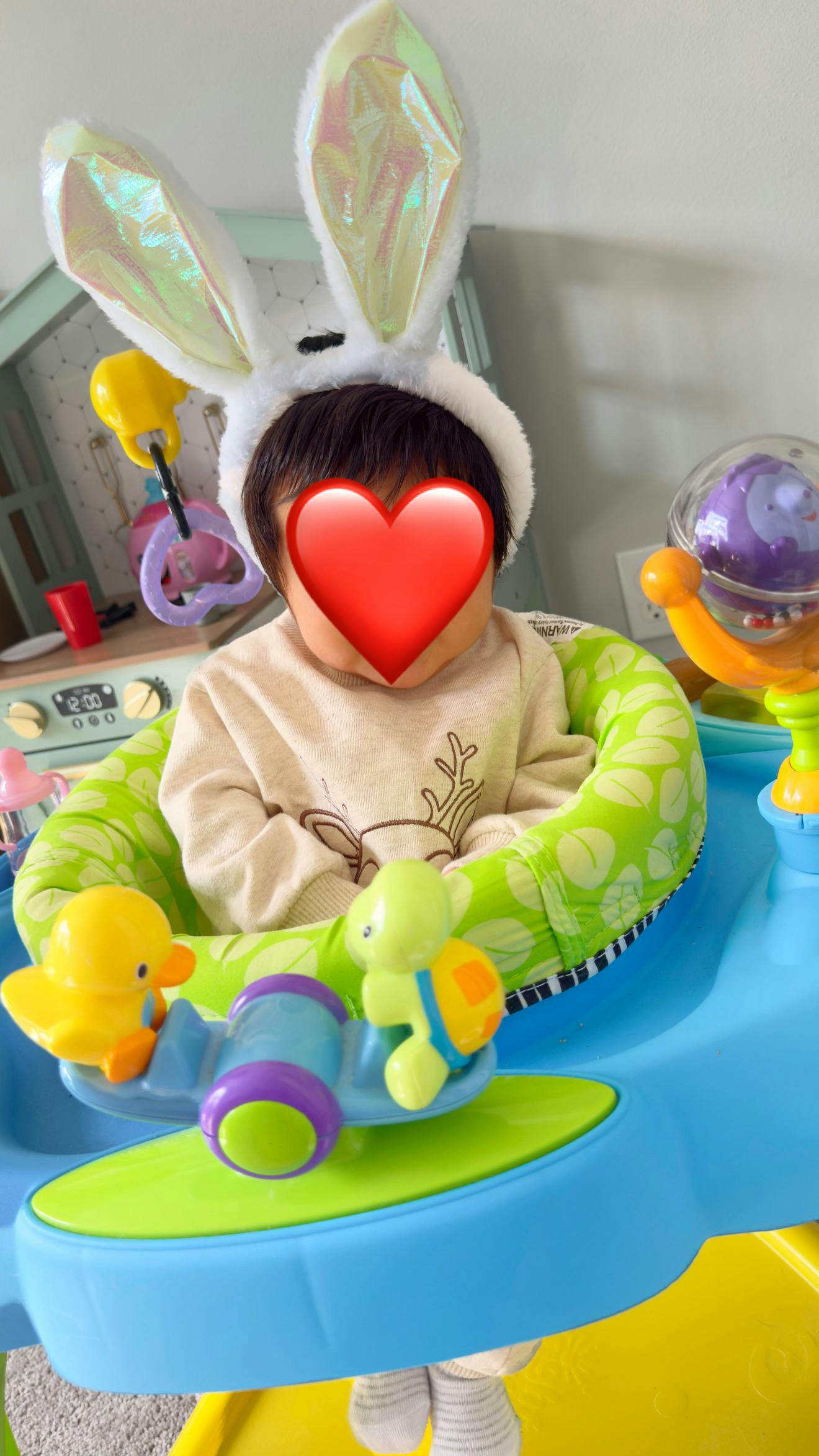 Child wearing bunny ears in a baby activity saucer