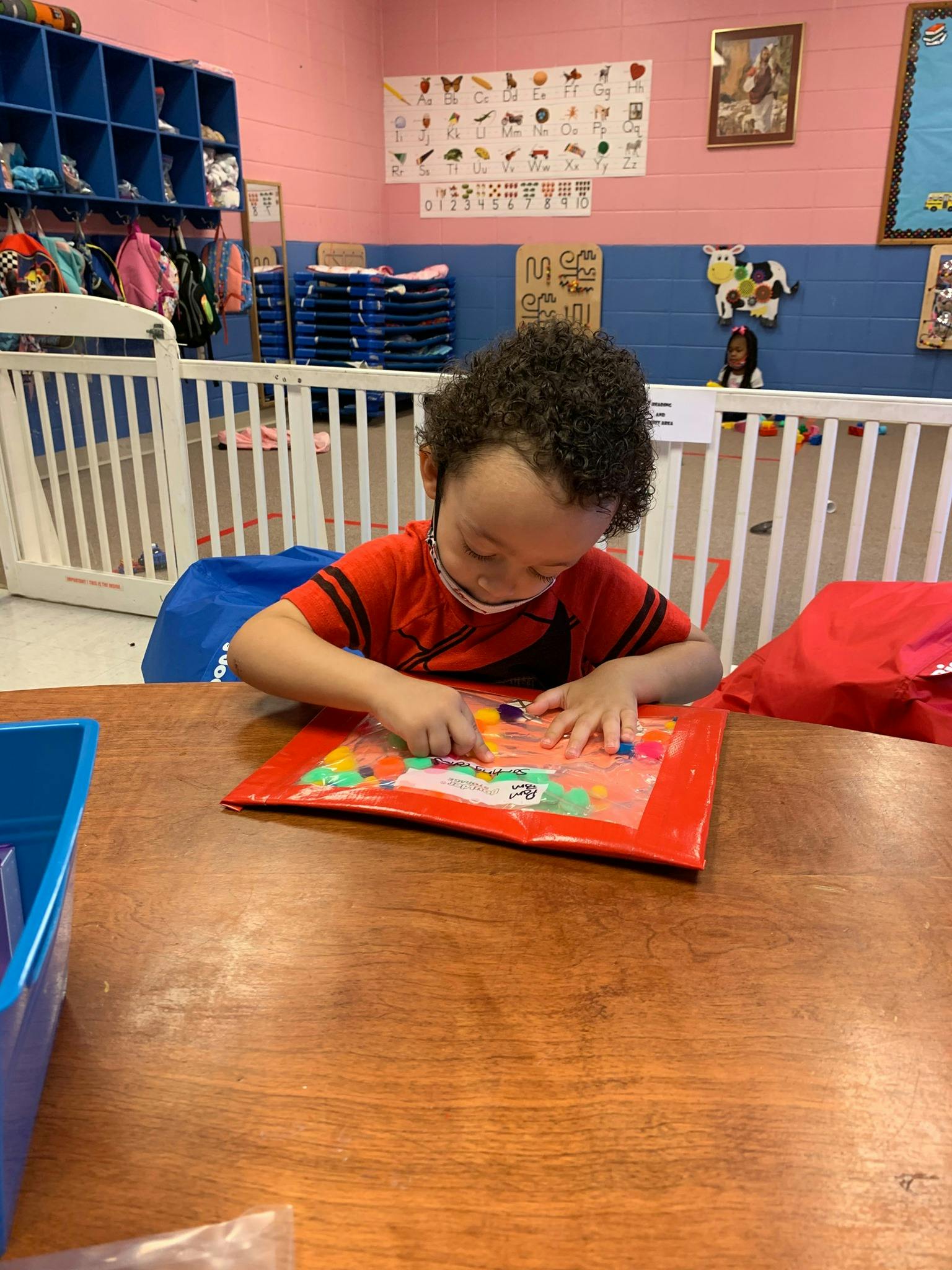 Child playing with colorful shapes on a red mat at a table