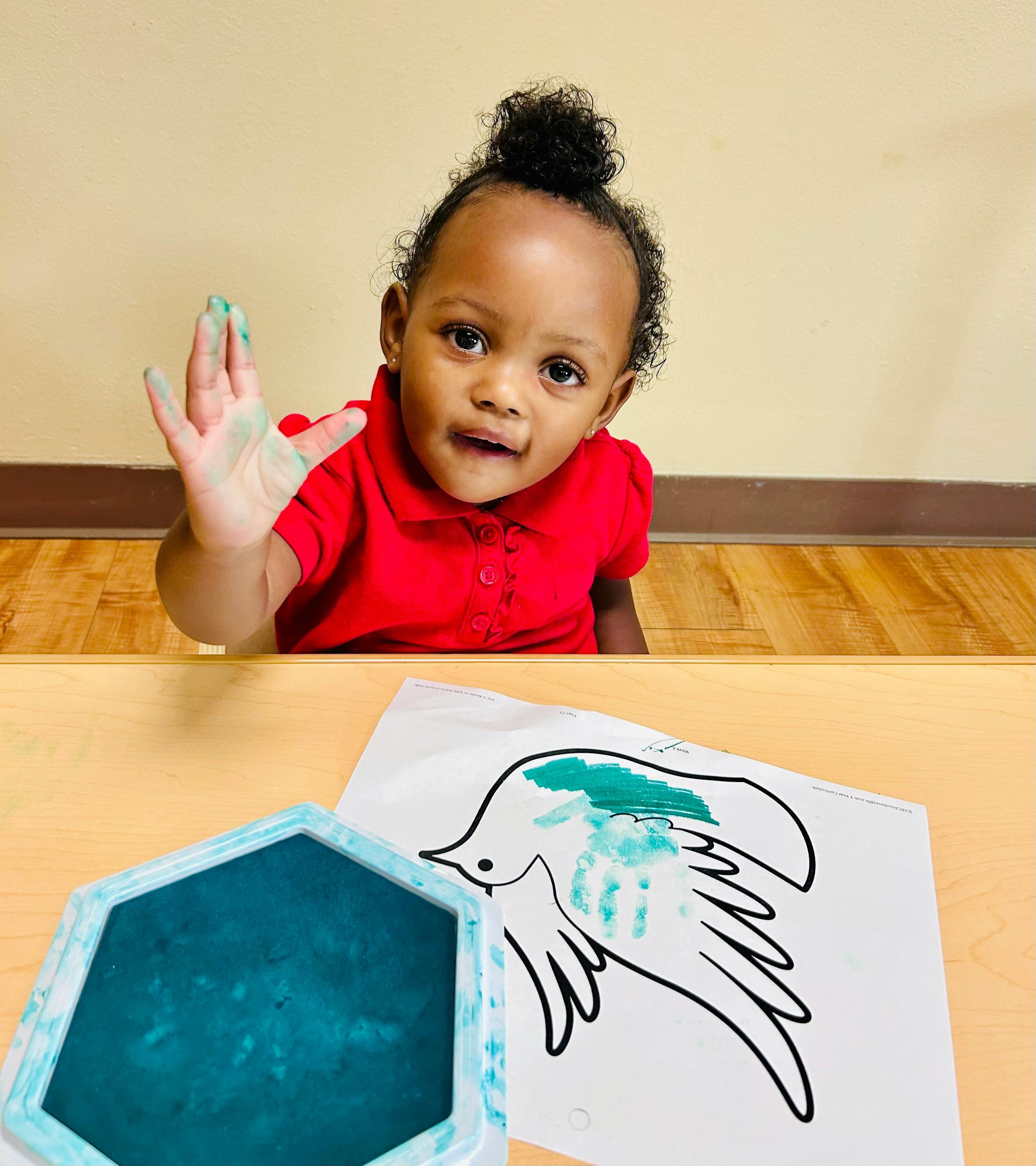 Child with paint on hand next to a bird drawing
