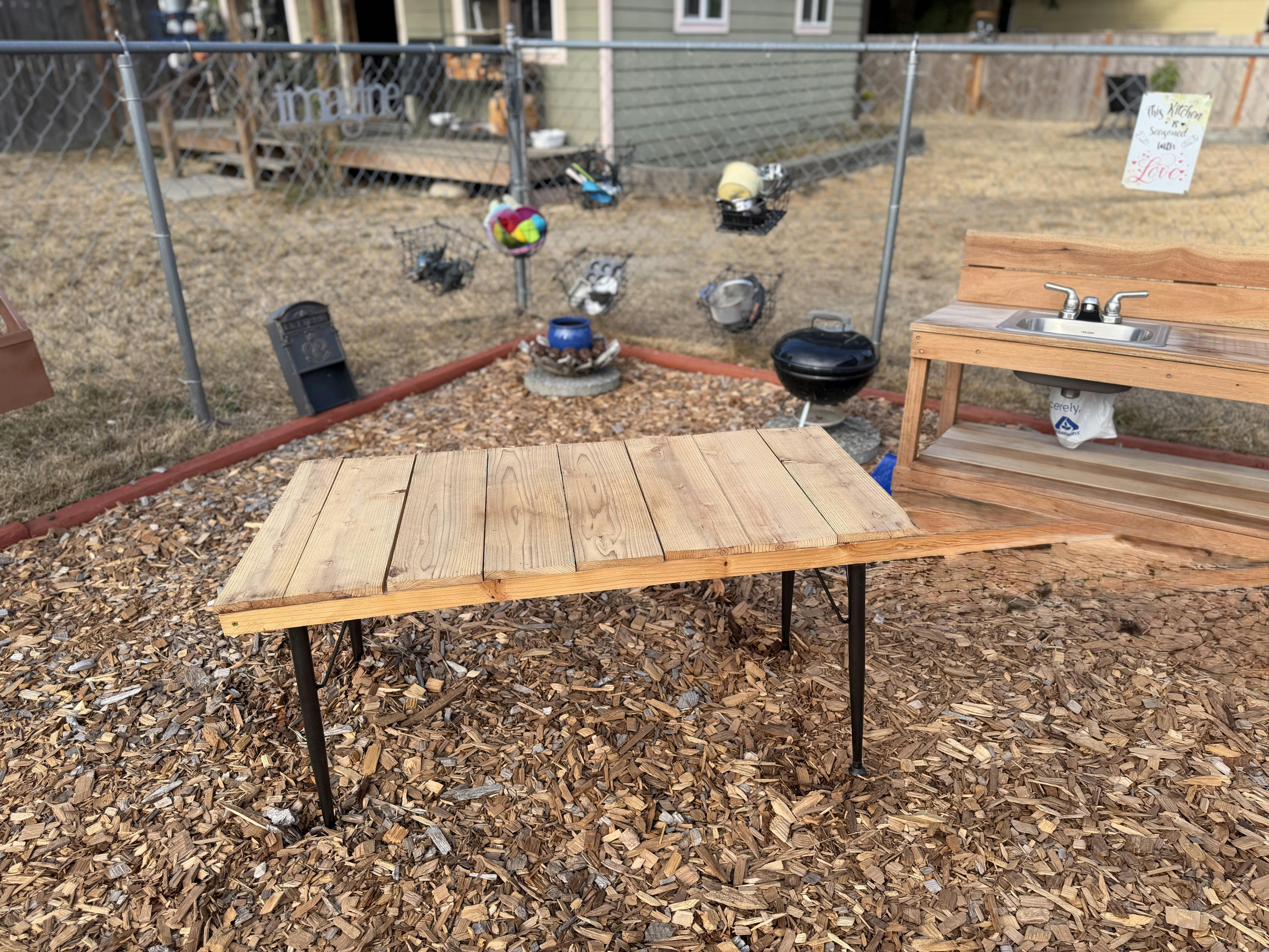 Wooden folding table in a backyard play area with a toy sink