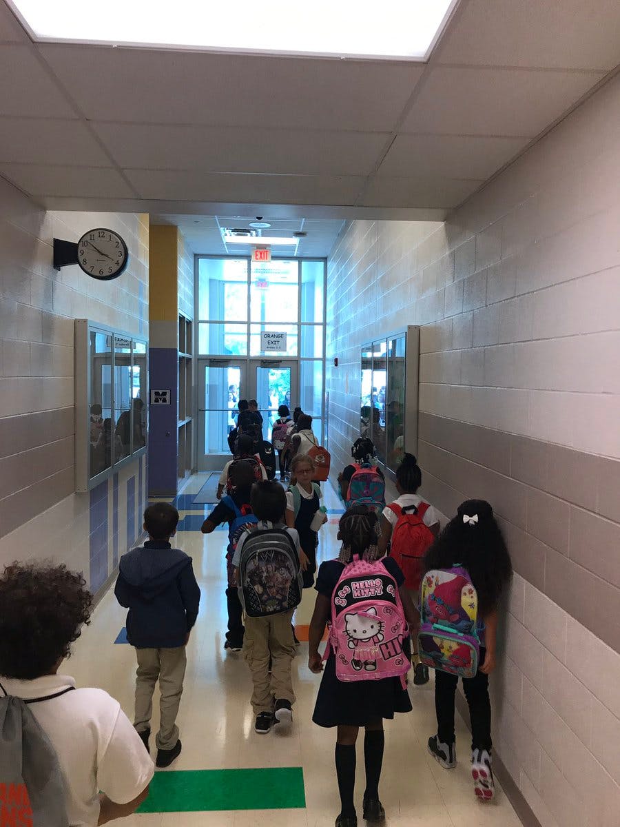Children walking down a school hallway with backpacks