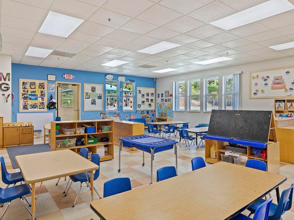 An empty classroom with small tables and chairs, and bright blue walls