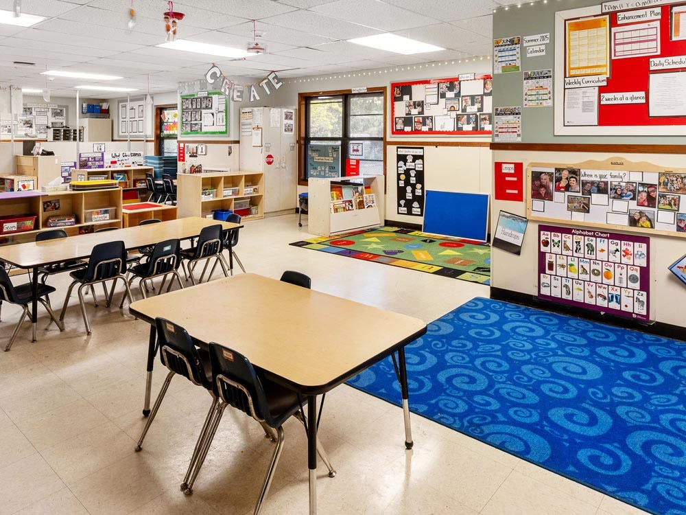 Empty classroom with small tables and chairs, bright rugs, and educational posters