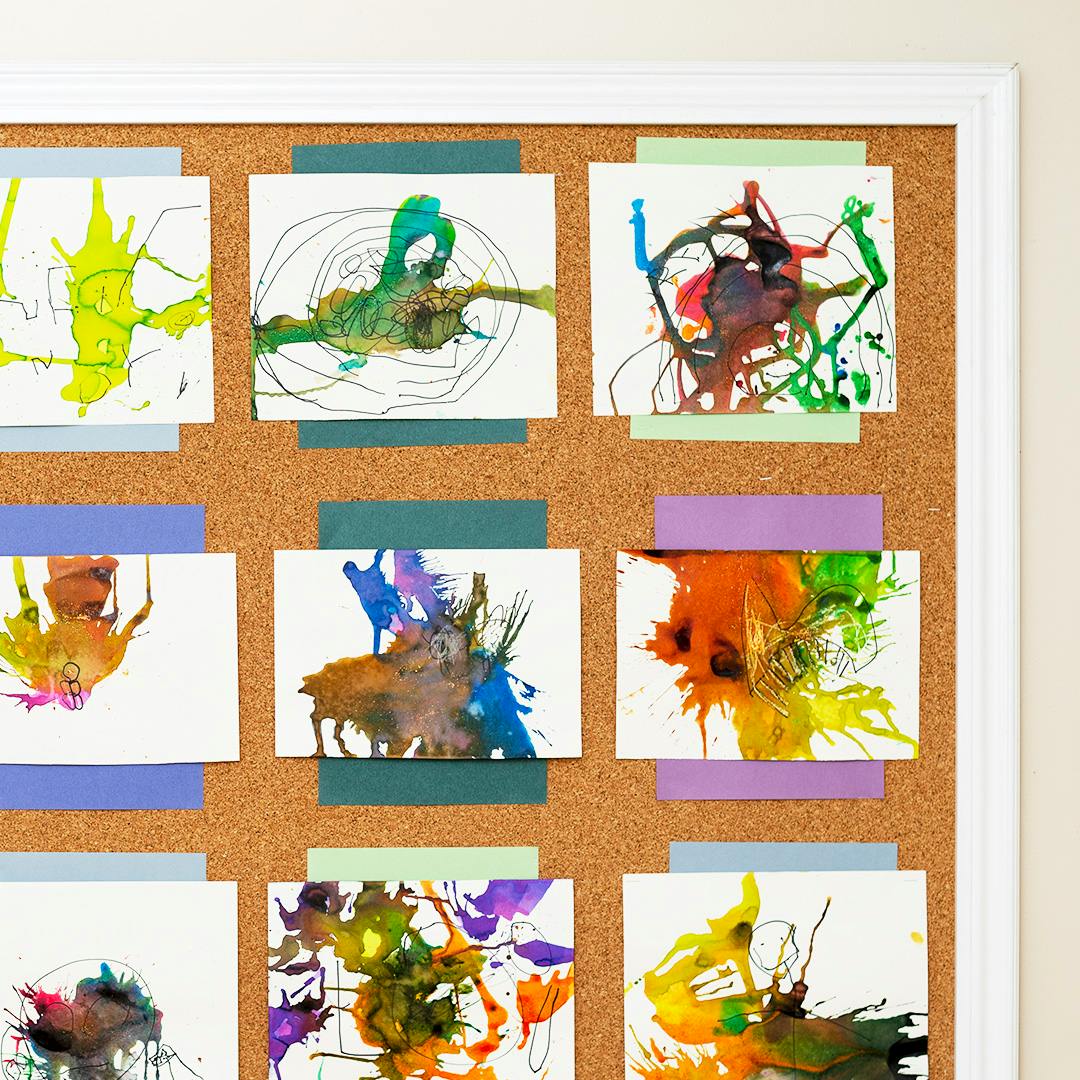 Children's artwork with colorful paint splatters on a cork board