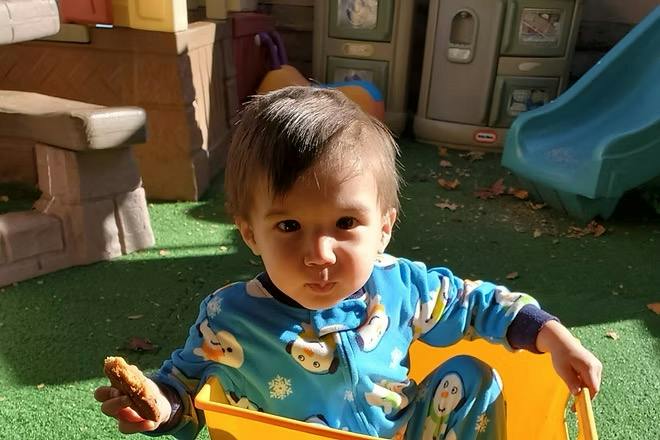 Child in blue pajamas eating a cookie while sitting in a yellow toy bin