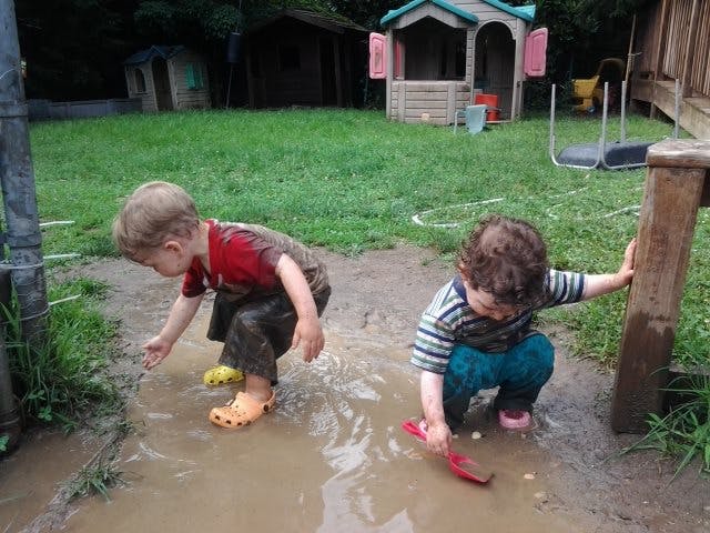 Two children playing in a muddy puddle