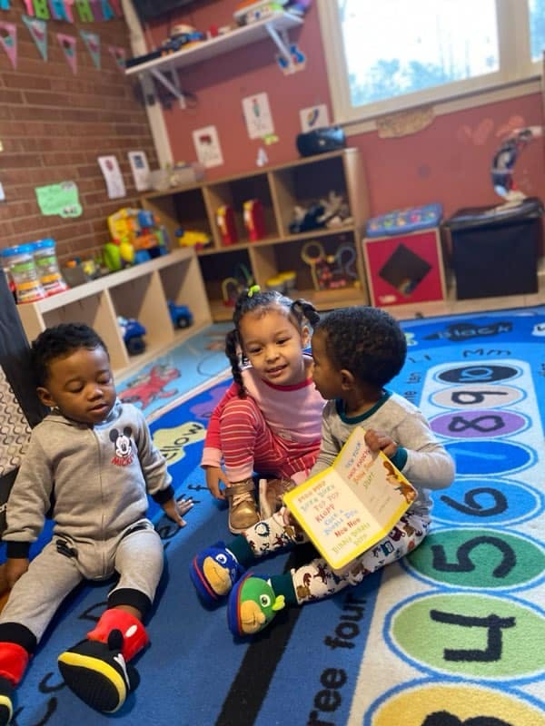 Three children sitting on a rug, one holding an open book