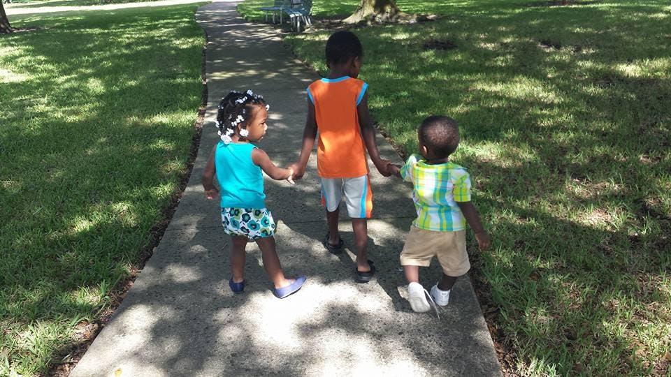 Three children walking on a sidewalk holding hands