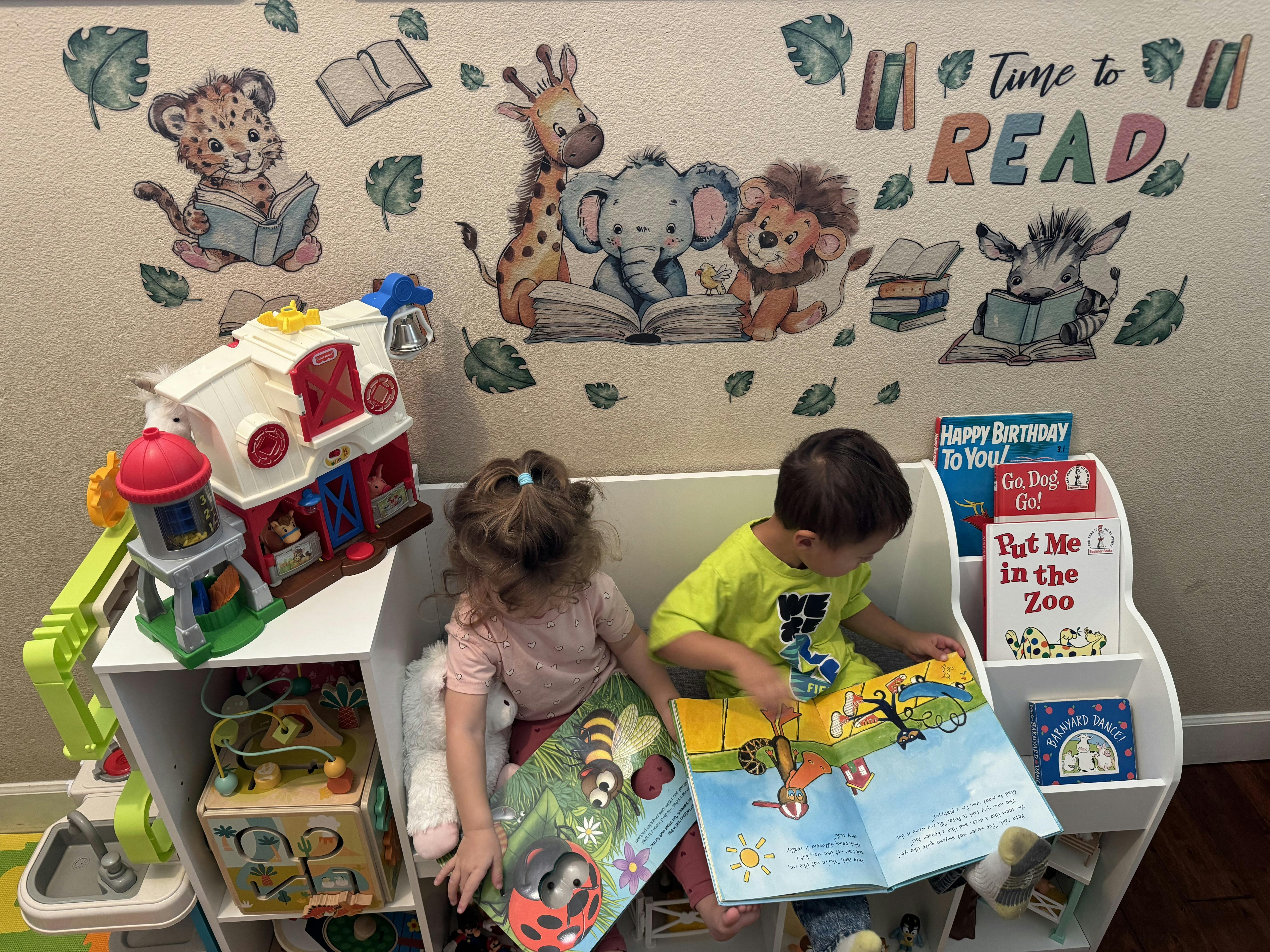 Two children sitting on a reading bench reading picture books