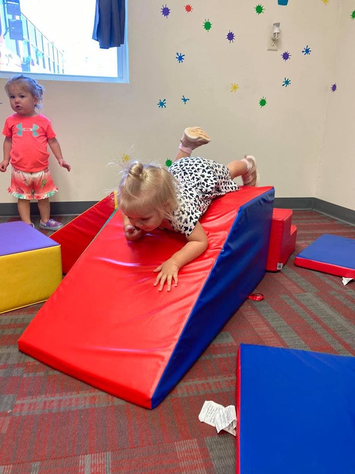 Child on a red and blue soft play slide, another child standing nearby