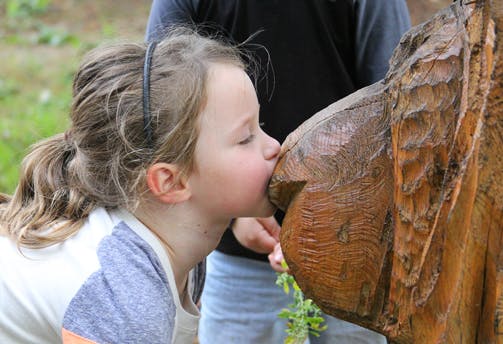 Child kissing a carved wooden animal