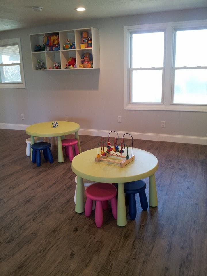 Two small round tables with colorful stools and toys in a room with windows