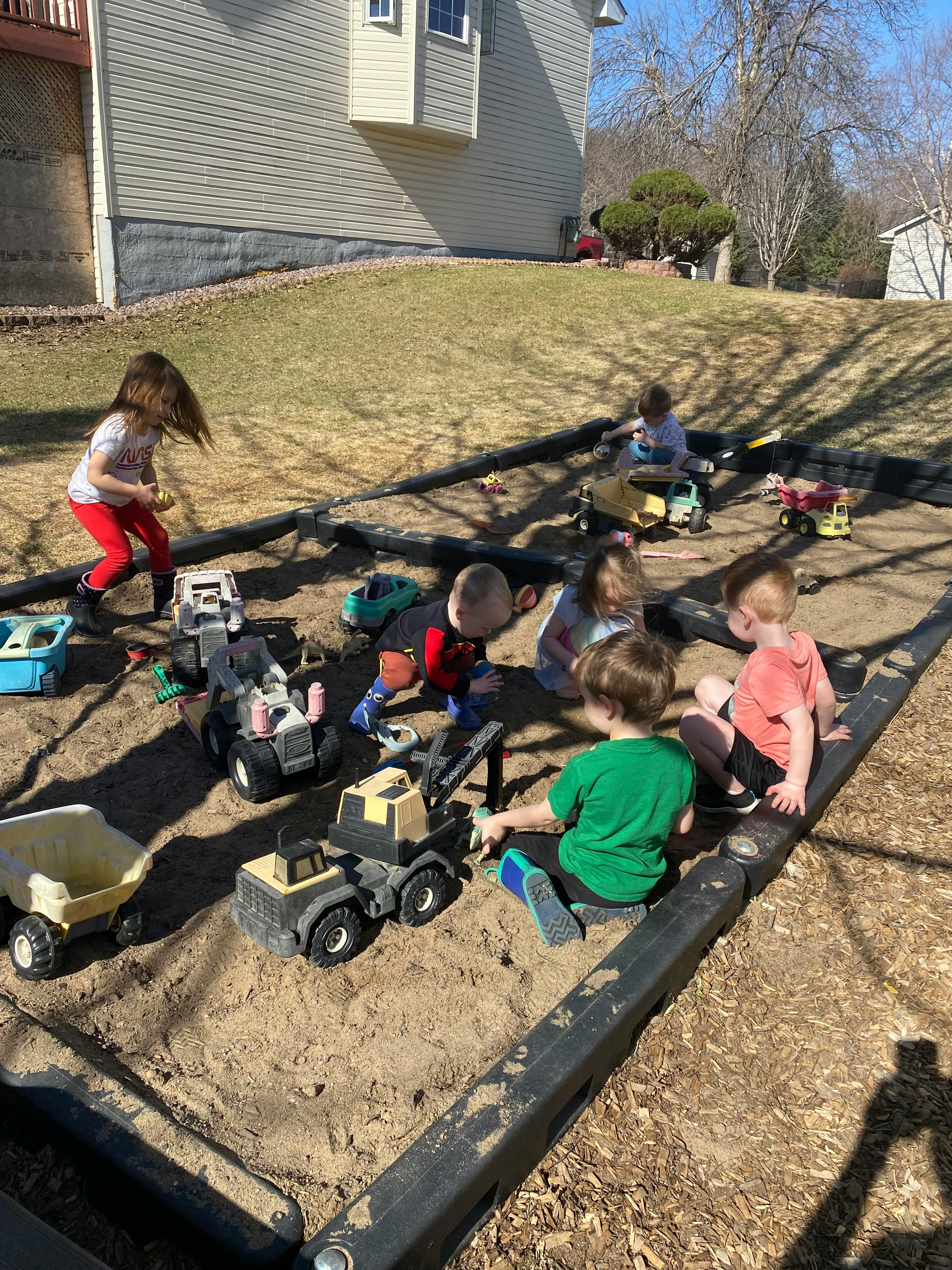 Children playing with toy trucks in a sandbox