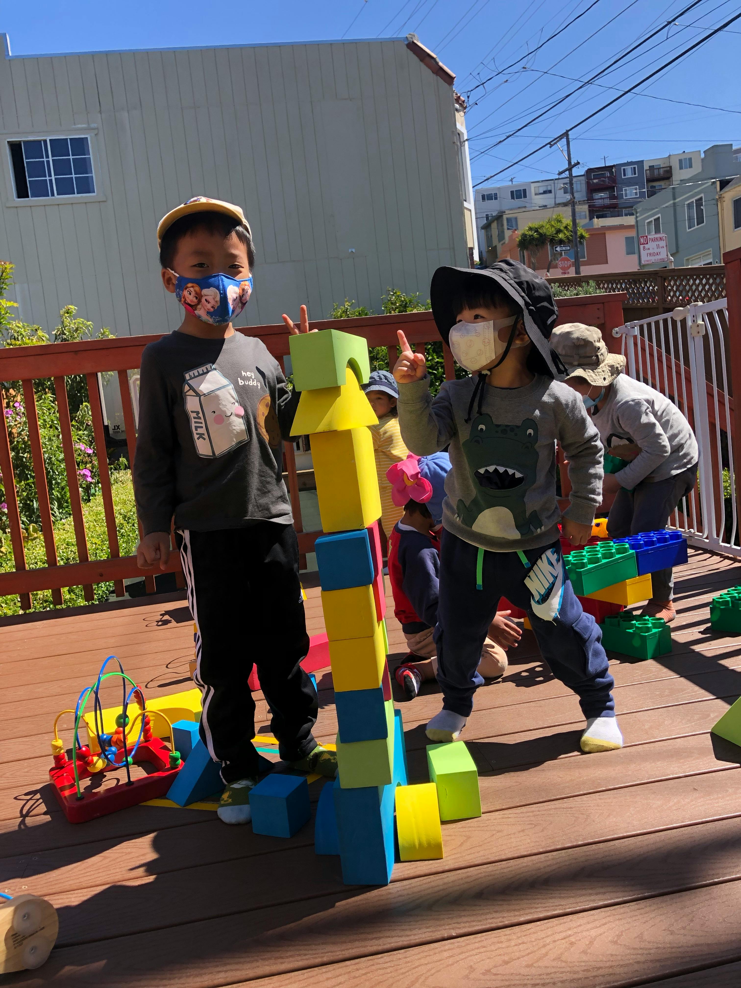 Two children in masks standing next to a tall tower of colorful blocks