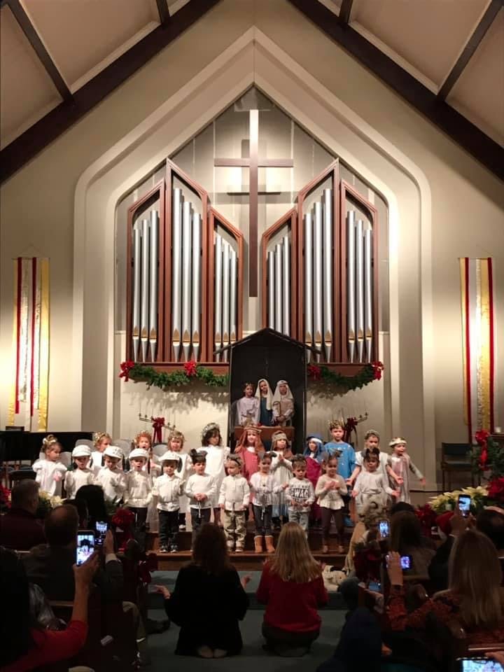 Children performing on a stage in a church with an organ and cross