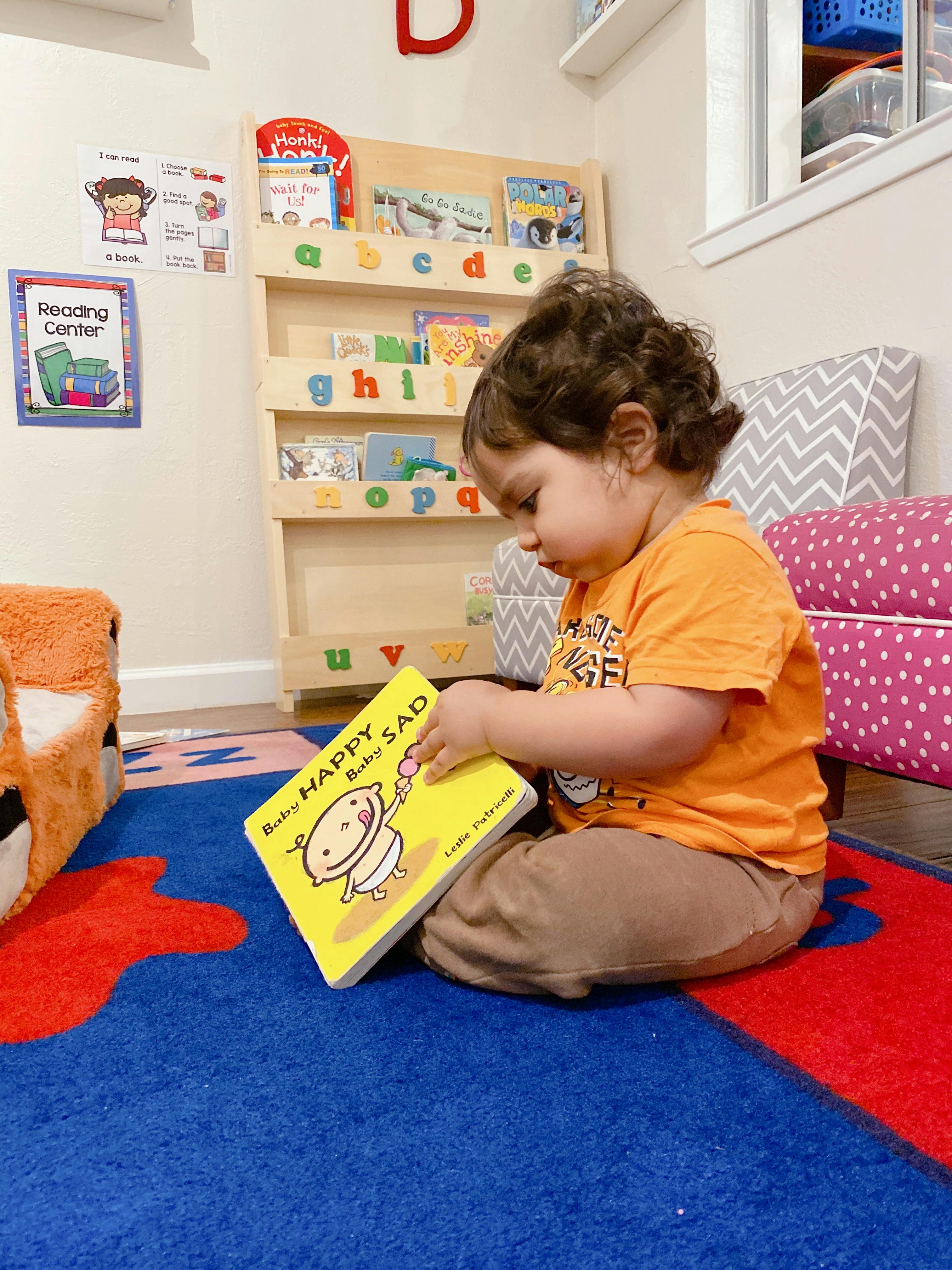 Child sitting on a rug, looking at a book titled "Happy Baby, Sad Baby"