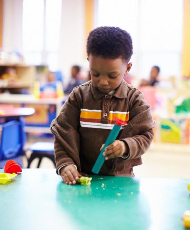 Child playing with modeling clay at a table in a classroom