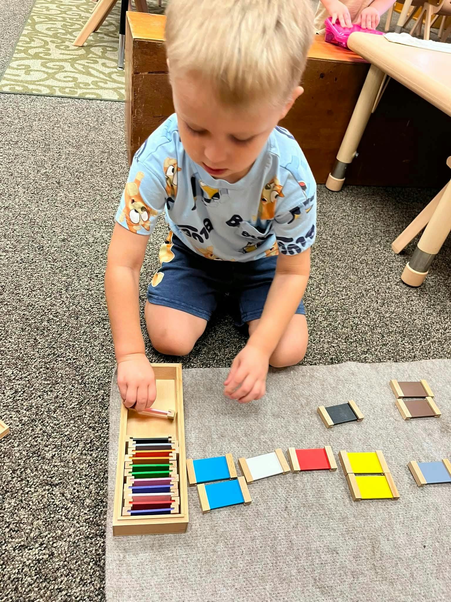 Child playing with a color tablet sorting activity on a classroom floor