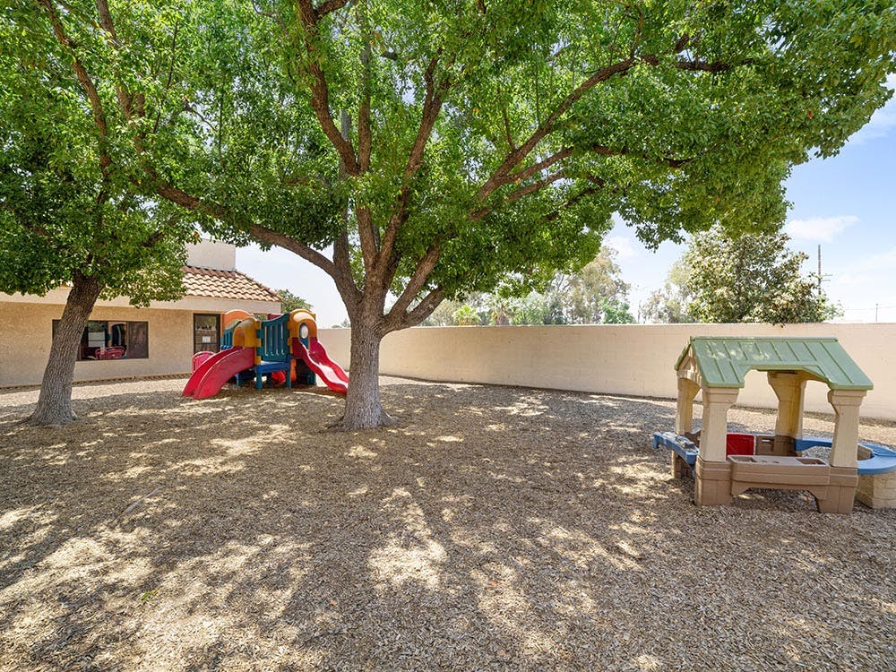 Outdoor playground with colorful slide structure and small play table under trees