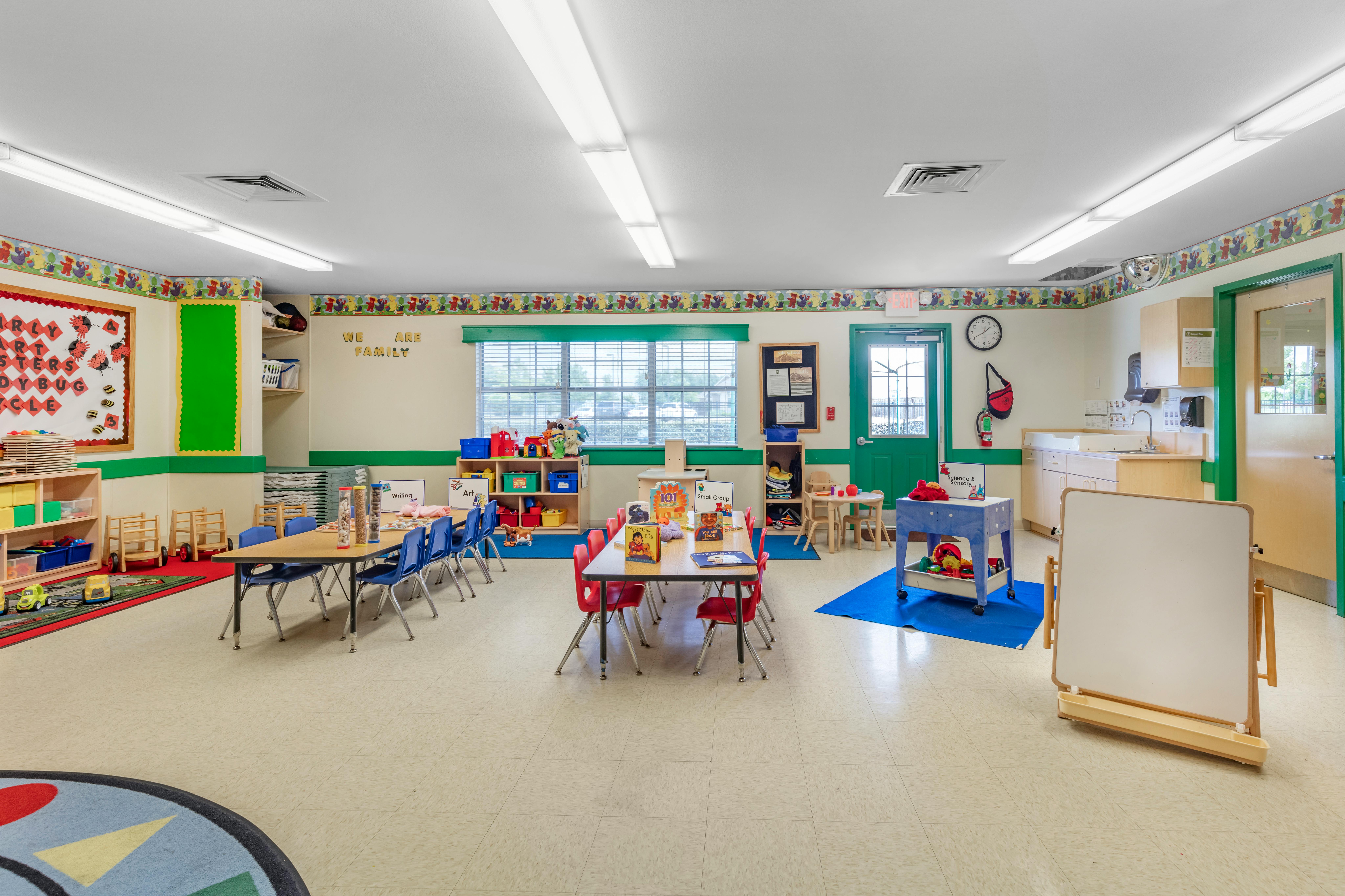 A classroom with small tables and chairs, shelves with toys, and various decorations