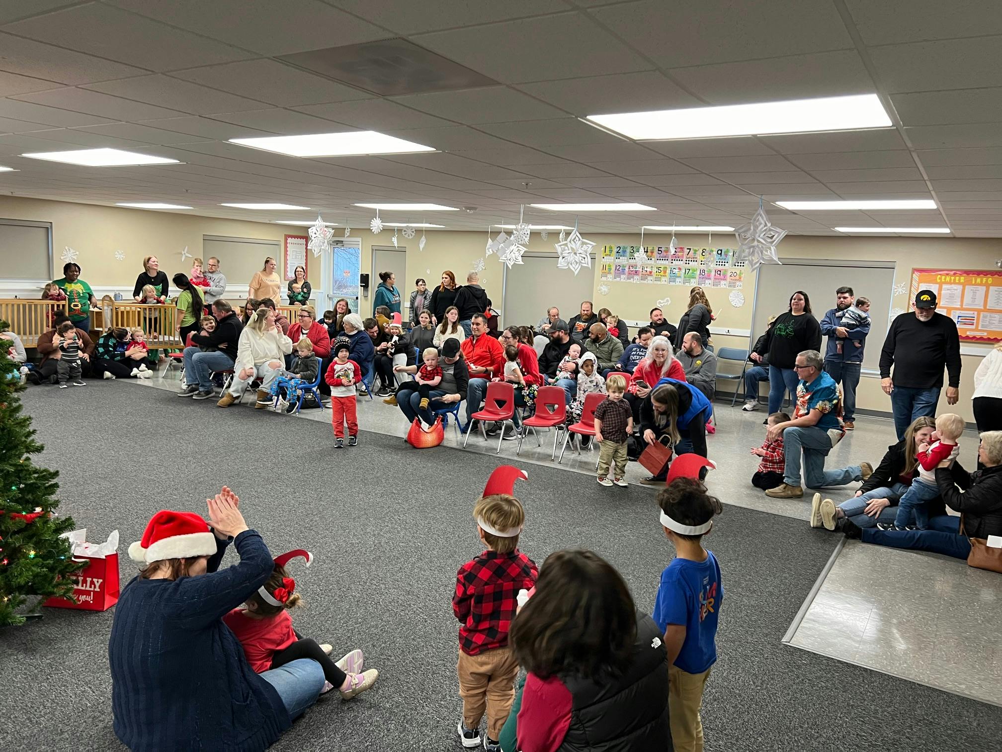 People and children gathered in a room, some wearing Santa hats