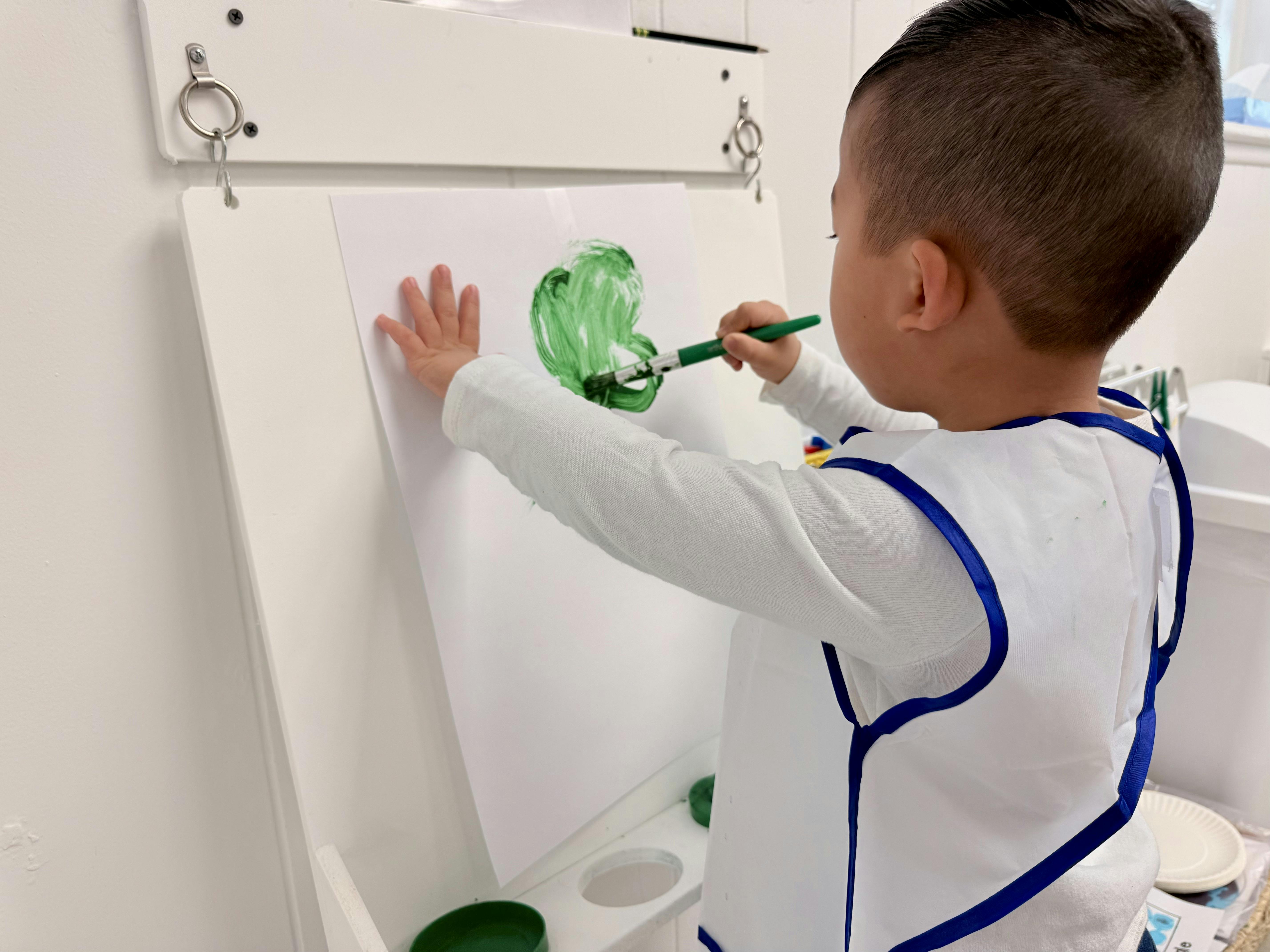 Child painting a green shape on an easel