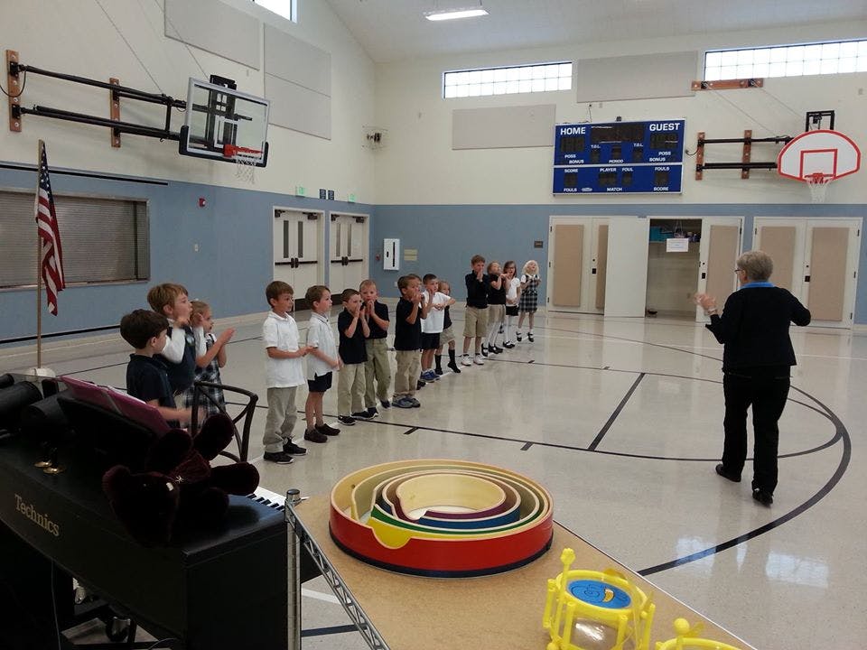 Children standing in a line in a gymnasium, facing a person