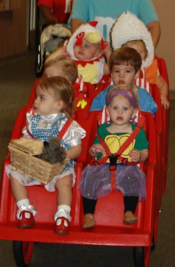 Multiple children in costumes riding in a red wagon