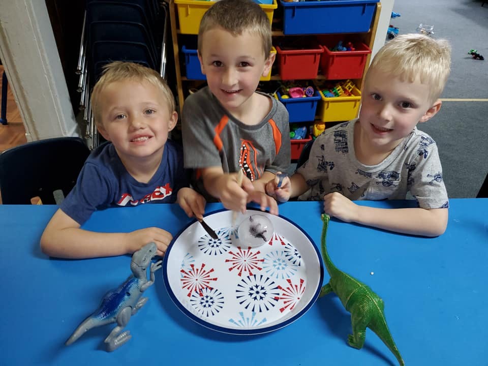 Three children at a table with a plate and toys