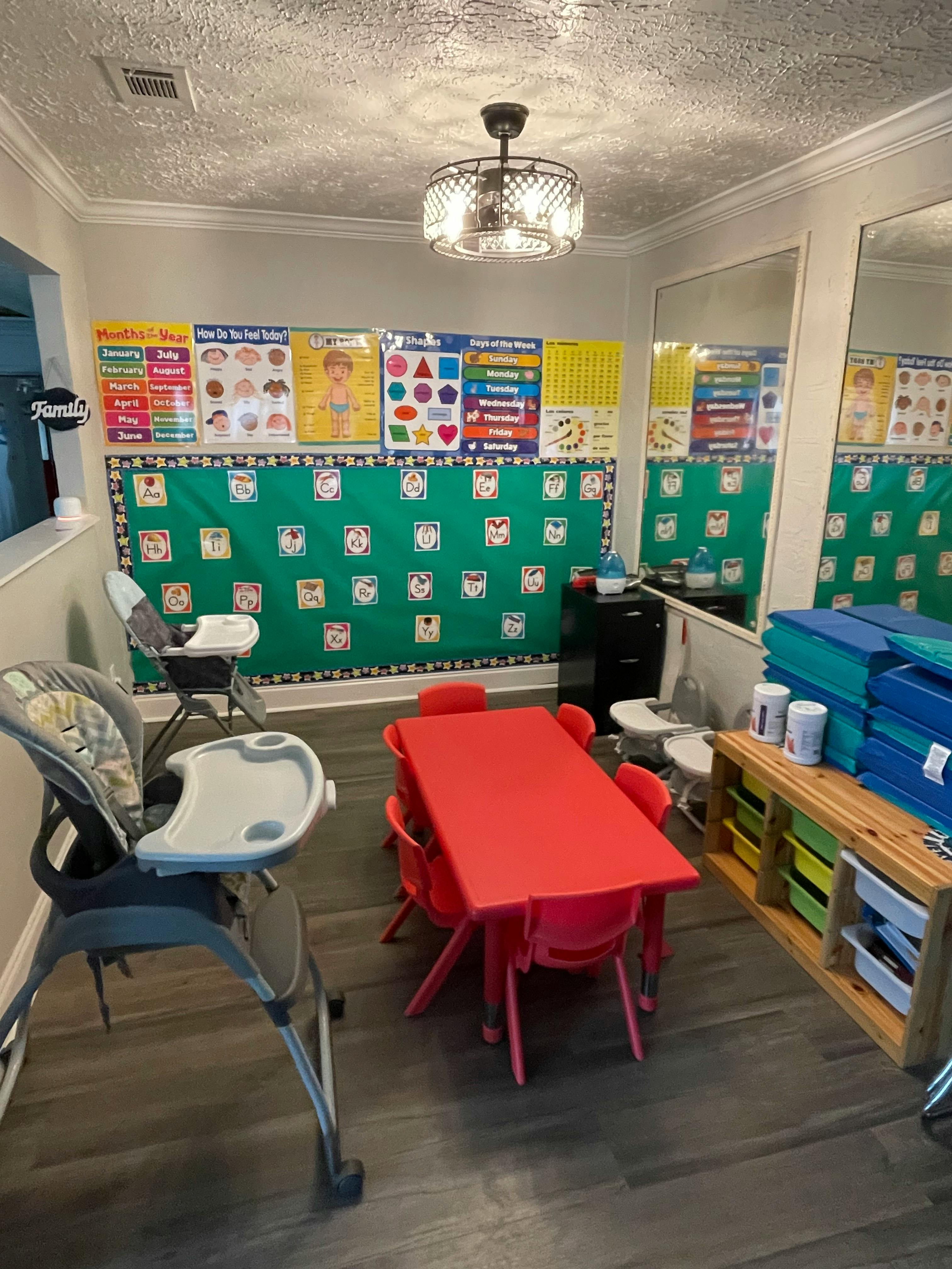 Classroom with red table and chairs, high chairs, and educational posters on wall