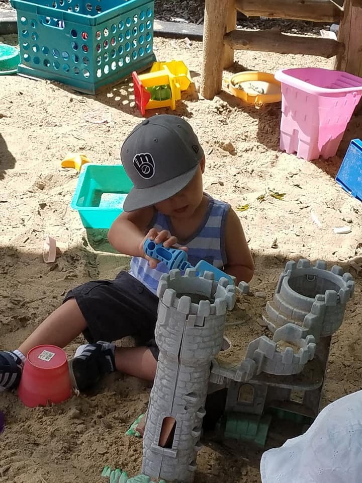 Child in a hat playing with sand toys and a castle in a sandbox