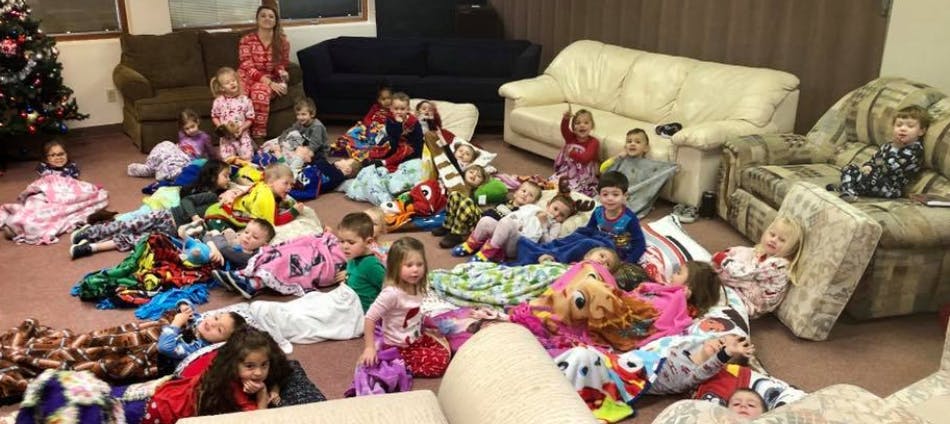 Many children and one adult sitting and lying on the floor with blankets