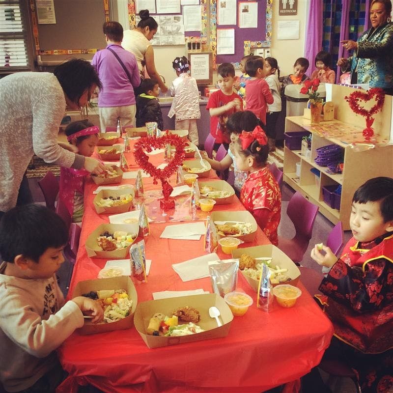 Adults and children eating at a long table with red tablecloths