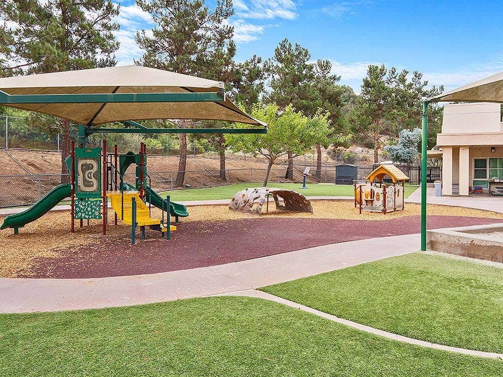 Playground with climbing structure, slides, shaded areas, and small playhouse