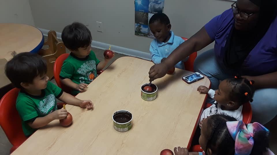 Adult and children at a table with small containers and apples