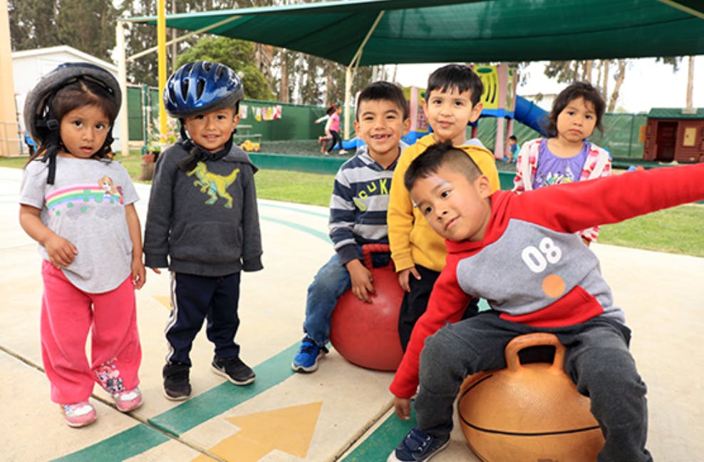 Group of children on a playground, some wearing helmets and sitting on hoppers